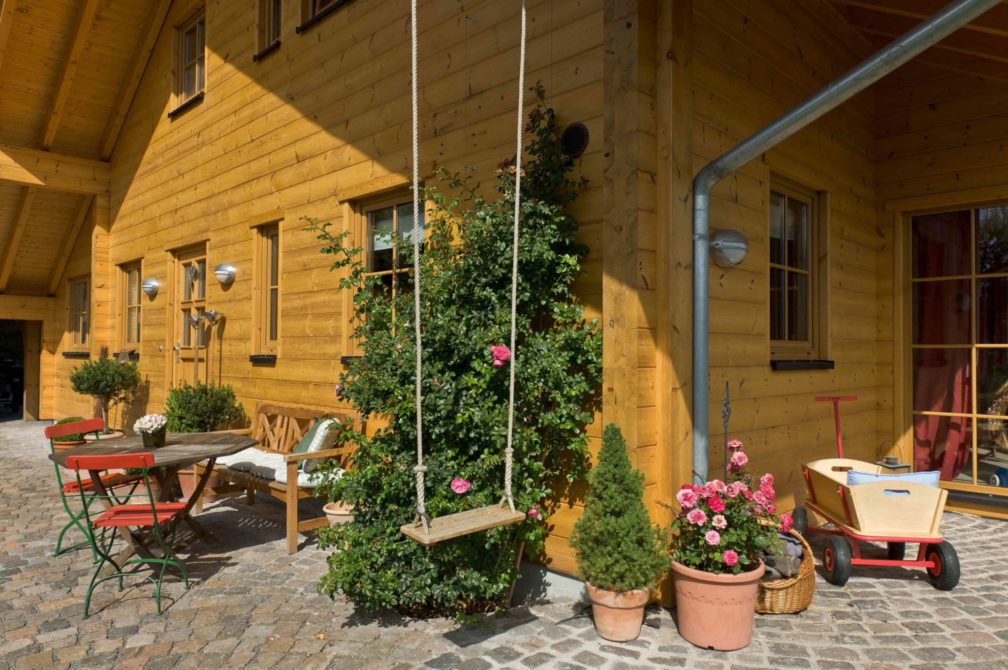 Landhaus aus Holz von Fullwood mit rotem Satteldach, honigfarbenen Blockbohlenwänden und weißen Sprossenfenstern in naturnaher Umgebung.